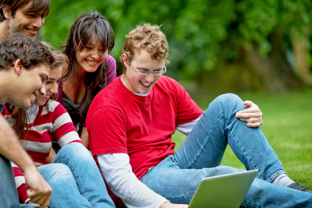 Group of friends with a laptop smiling outdoors